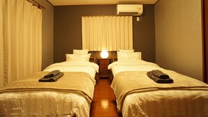 A hotel room with two beds, a nightstand, an air conditioning unit, and a window with curtains. - PINK Suite HOUSE (Nanjo)