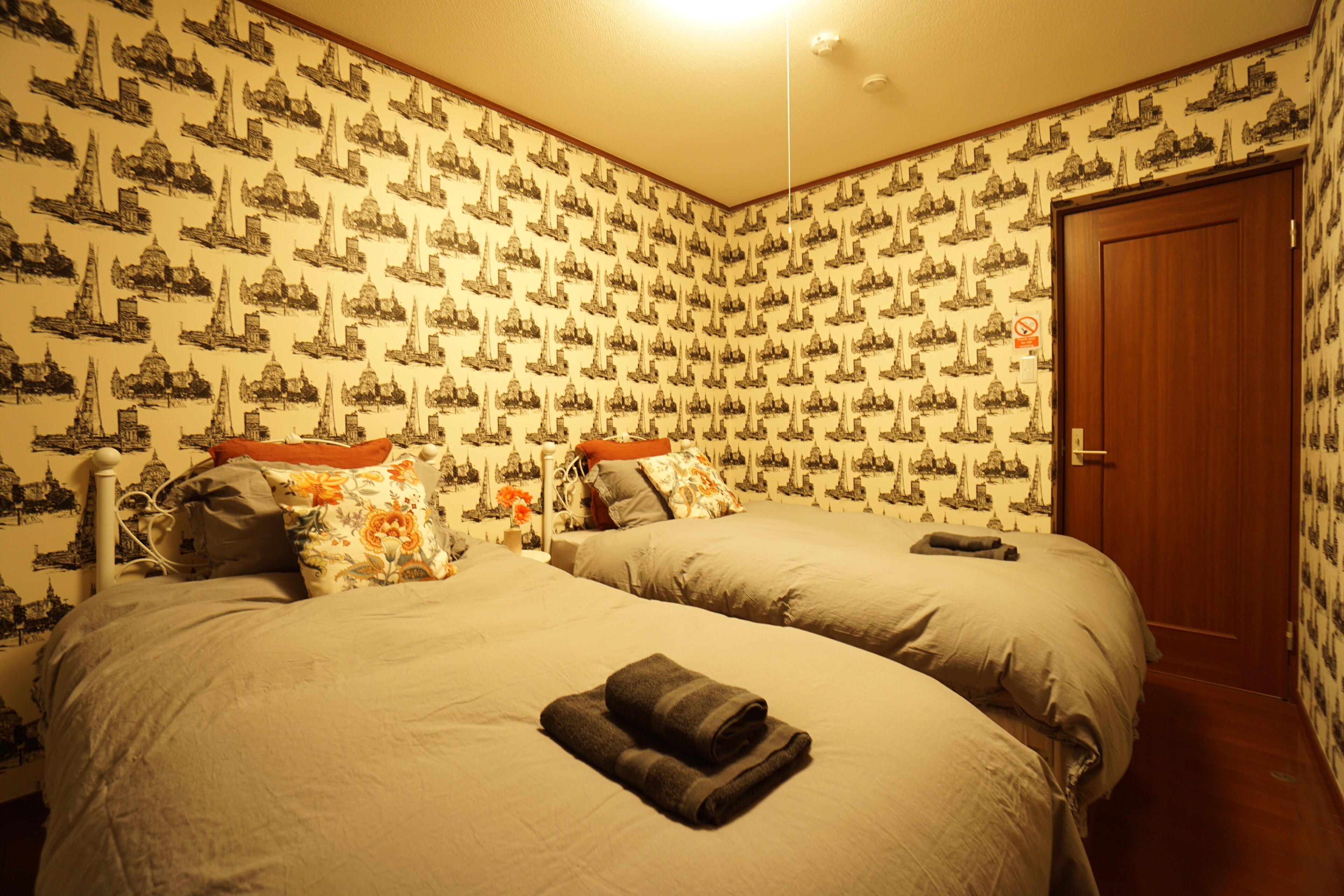 A room with two beds, a wooden door, and patterned wallpaper.