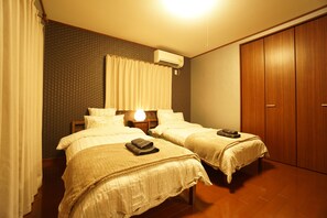 A room with two beds, a wardrobe, and an air conditioning unit.