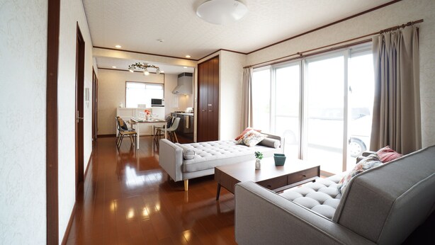 A spacious living room with a sofa, a coffee table, and a dining area with chairs and a table. - PINK Suite HOUSE (Nanjo)
