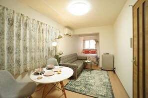 A compact living space with a dining area, a sofa, a radiator, and a small table with a lamp. - Kikusui Mark's apartment (Sapporo)
