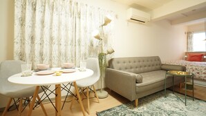 A modern living room with a round dining table, two chairs, a sofa, a small side table, and a floor lamp. - Kikusui Mark's apartment (Sapporo)