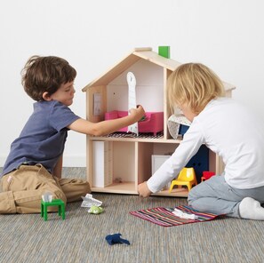 Two children playing with a dollhouse on a carpeted floor.