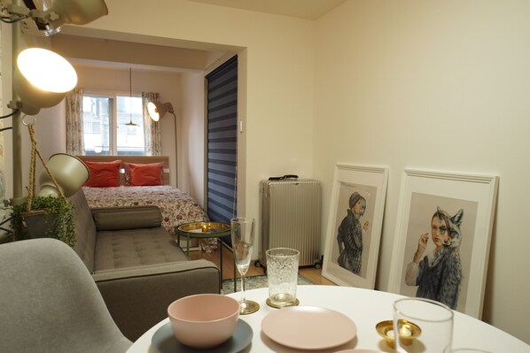 A cozy room with a bed, a small table with a bowl and glass, a radiator, and framed pictures on the wall.