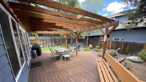 Un terrazzo in legno con una pergola, arredi da esterno e un barbecue.