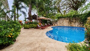 A curved swimming pool with lounge chairs and umbrellas, surrounded by lush greenery and a stone wall. - Hemingway House by Blue Sky Luxury (Mullins)
