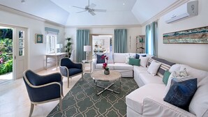 A spacious living room with a ceiling fan, a white sofa, a blue armchair, and a coffee table with a vase of flowers. - Porters Villa by Blue Sky Luxury (Holetown)
