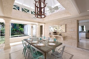 Une salle à manger spacieuse avec un plafond haut, une grande fenêtre et une vue sur un jardin.