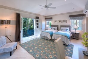 Une chambre avec deux lits, un ventilateur de plafond, une grande fenêtre et une vue sur la verdure.