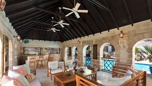 An outdoor patio with wooden furniture, ceiling fans, and a pool view. - Porters Villa by Blue Sky Luxury (Holetown)