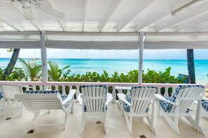 A covered outdoor seating area with white chairs and a view of the ocean.