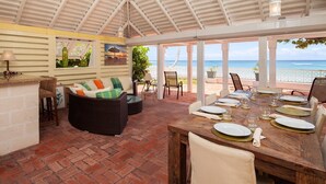 A covered outdoor dining area with a brick floor, a wooden table set for four, and a view of the ocean. - Arcadia by Blue Sky Luxury (Worthing)