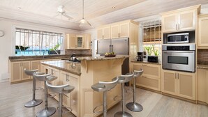 A kitchen with a central island, bar stools, stainless steel appliances, and a view of the outdoors. - Arcadia by Blue Sky Luxury (Worthing)