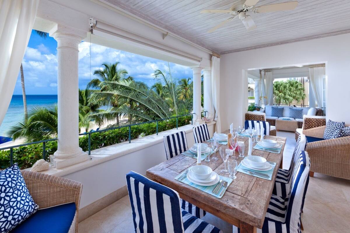 A dining area with a view of the ocean, white columns, striped chairs, and wicker furniture.