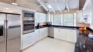 Una cocina moderna con electrodomésticos de acero inoxidable, armarios blancos y un ventilador de techo.