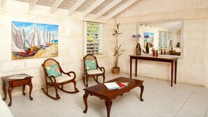 Una habitación con techo de madera, un cuadro de veleros, dos mecedoras, una mesita de centro, un espejo y una planta en maceta.