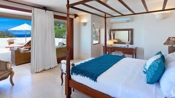A four-poster bed with a blue throw, a wooden nightstand, a mirror, and a view of the ocean.