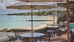 An outdoor seating area with round tables and chairs, overlooking a beach and the sea. - Tom Tom by Blue Sky Luxury (Westmoreland)