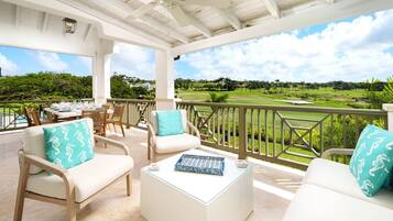 A covered outdoor seating area with wicker furniture, a glass coffee table, and a view of a golf course.