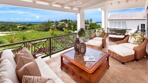 A spacious balcony with wicker furniture, a glass-top coffee table, and a view of a lush landscape. - Royal Westmoreland - Sugar Cane Ridge by Blue Sky Luxury (Holetown)