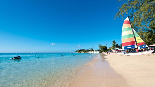 A beach with clear turquoise water, a sandy shore, and a colorful sailboat. - Royal Westmoreland - Sugar Cane Ridge by Blue Sky Luxury (Holetown)
