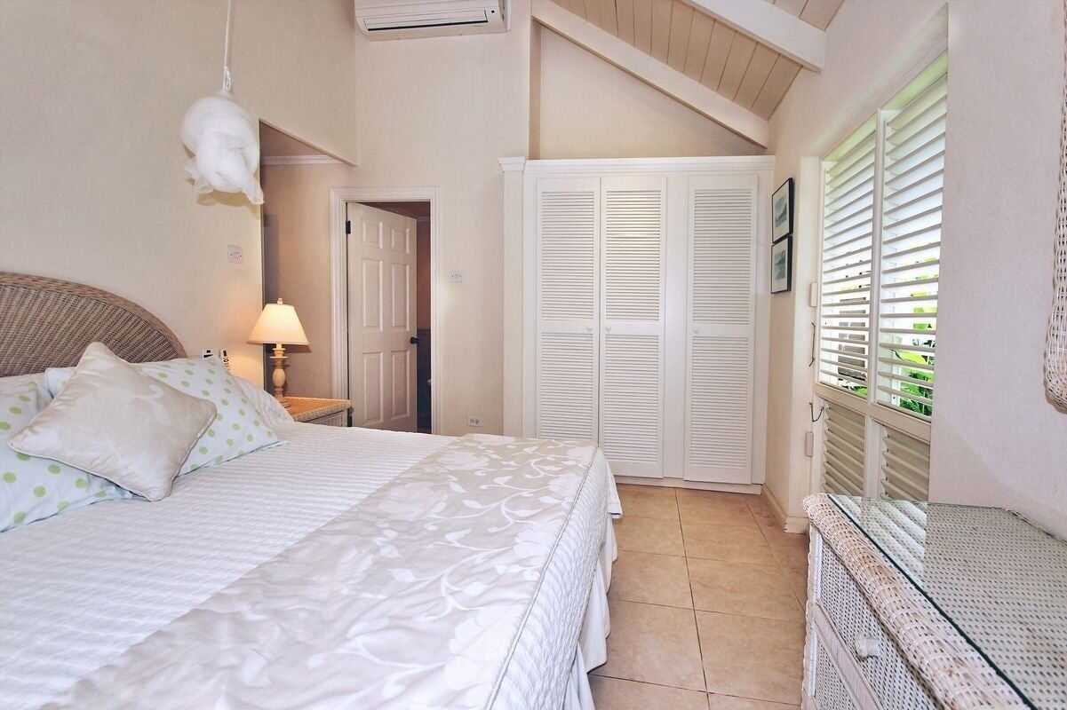 A bedroom with a bed, a nightstand, a lamp, a wardrobe, and a window with blinds.
