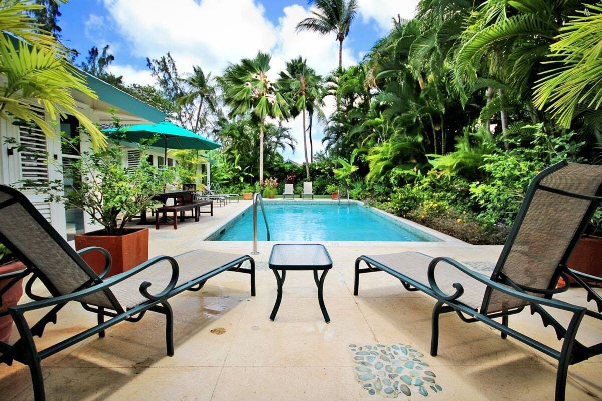 Un espace piscine avec des chaises longues, une table et un bâtiment doté d’un auvent vert.