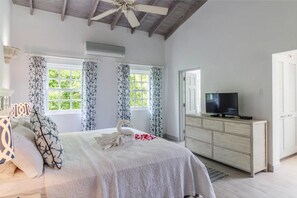 A bedroom with a bed, a television on a dresser, and two windows with curtains. - Westshore Beach House by Blue Sky Luxury (Holetown)