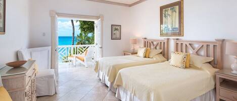 A hotel room with two beds, a ceiling fan, a balcony with a view of the ocean, and a door leading outside.