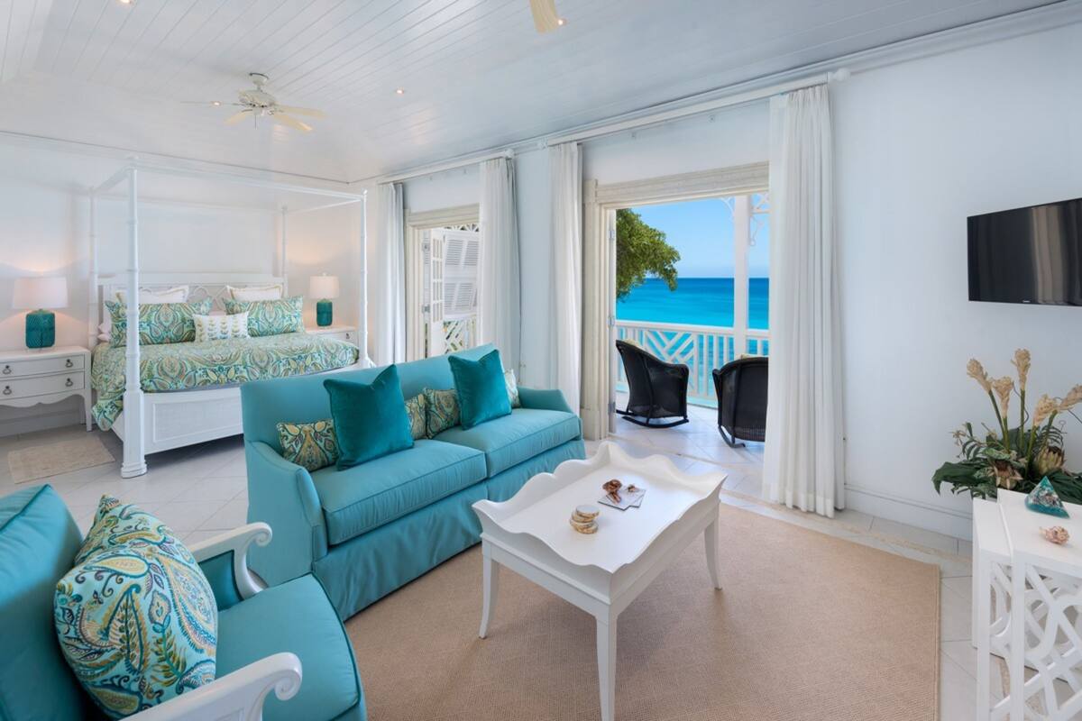 A spacious room with a bed, a teal sofa, a white coffee table, and a balcony with a view of the sea.