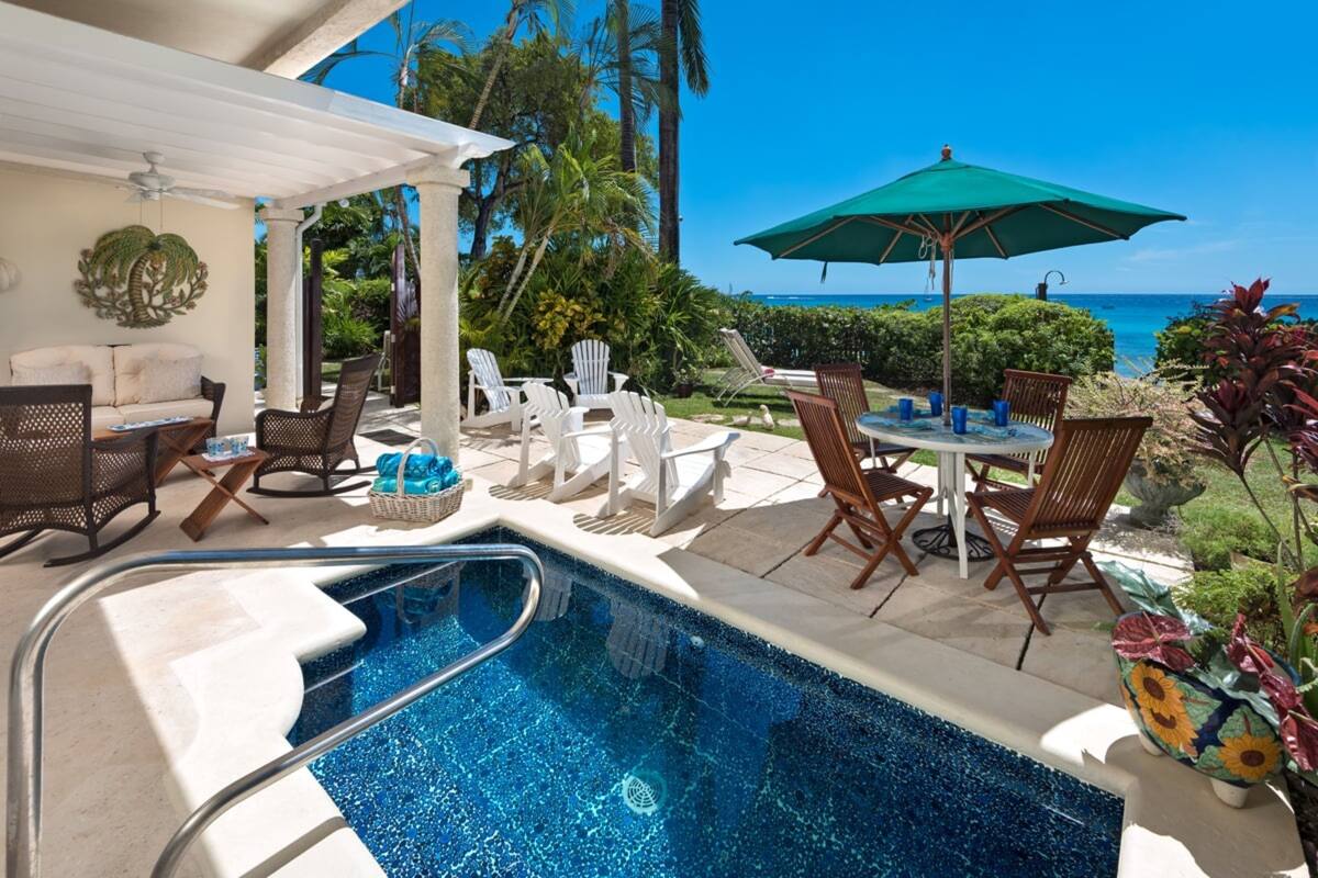 A pool area with lounge chairs and a table, overlooking a scenic ocean view.