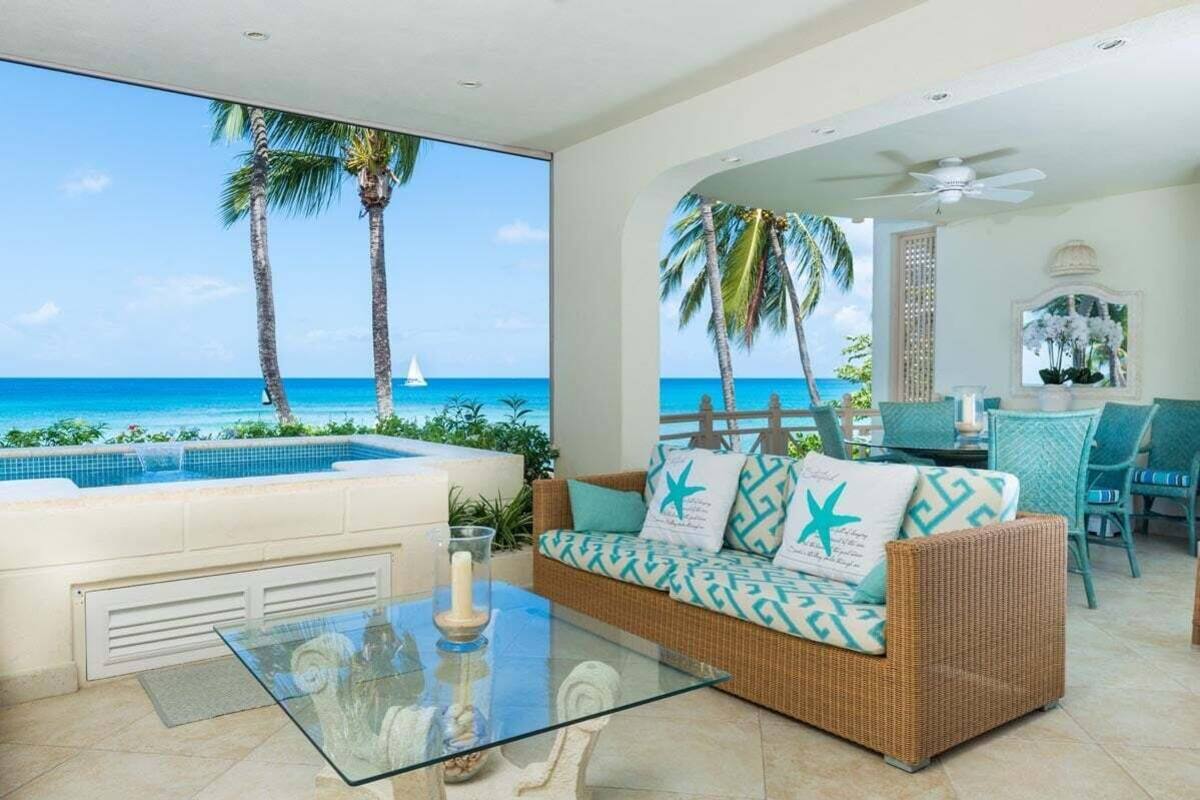 A room with a glass table, wicker sofa, and a view of the ocean.
