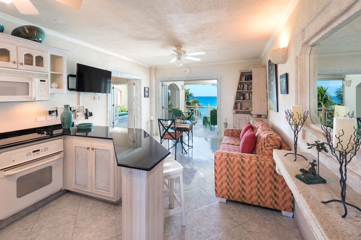 A modern kitchen with a flat-screen TV, white cabinetry, and a dining area with a view of the ocean.
