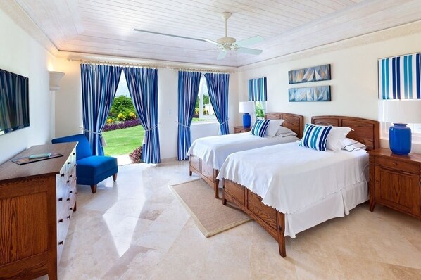 A bedroom with two beds, a desk, and a view of the garden.