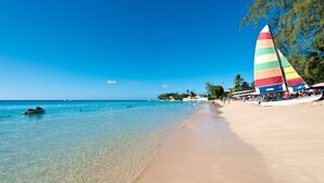 A beach with a sailboat, clear water, and a sandy shore. - Royal Westmoreland - High Spirit by Blue Sky Luxury (Westmoreland)