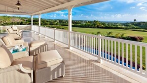 A covered outdoor seating area with wicker furniture and a view of a golf course. - Royal Westmoreland - High Spirit by Blue Sky Luxury (Westmoreland)