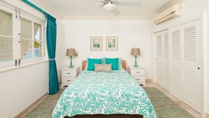 A bedroom with a bed, nightstands, a ceiling fan, and a window with curtains. - Waterside 402 by Blue Sky Luxury (Paynes Bay)