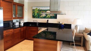A modern kitchen with wooden cabinets, a black countertop, and a central island. - Waterside 402 by Blue Sky Luxury (Paynes Bay)