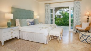 A bedroom with a large bed, two bedside tables, a bench, a chair, and a view of the outdoors through a glass door. - Schooner Bay 205 by Blue Sky Luxury (Speightstown)