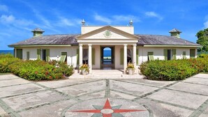 Un bâtiment de style colonial, doté d’une façade symétrique, d’une entrée centrale et d’un jardin aménagé avec un motif en forme de boussole incrusté dans le sol.
