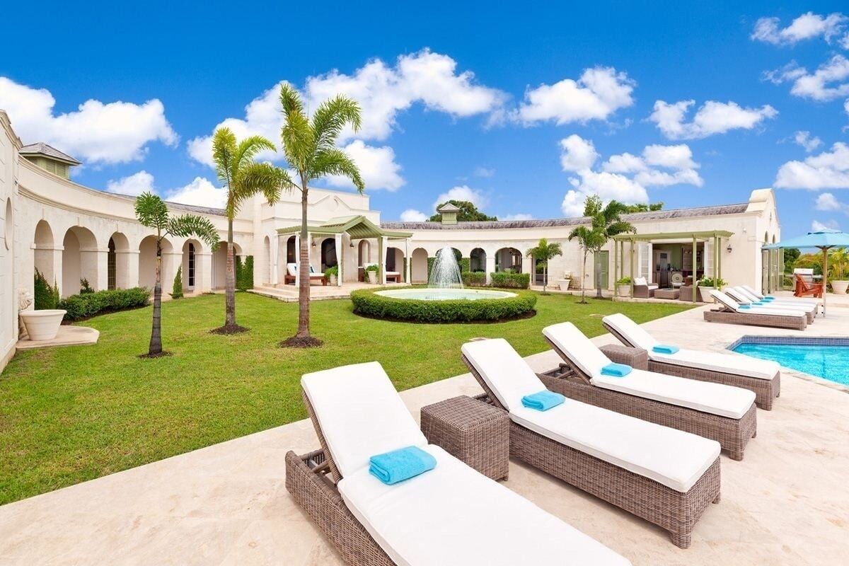 A resort courtyard with lounge chairs, a swimming pool, and a fountain.