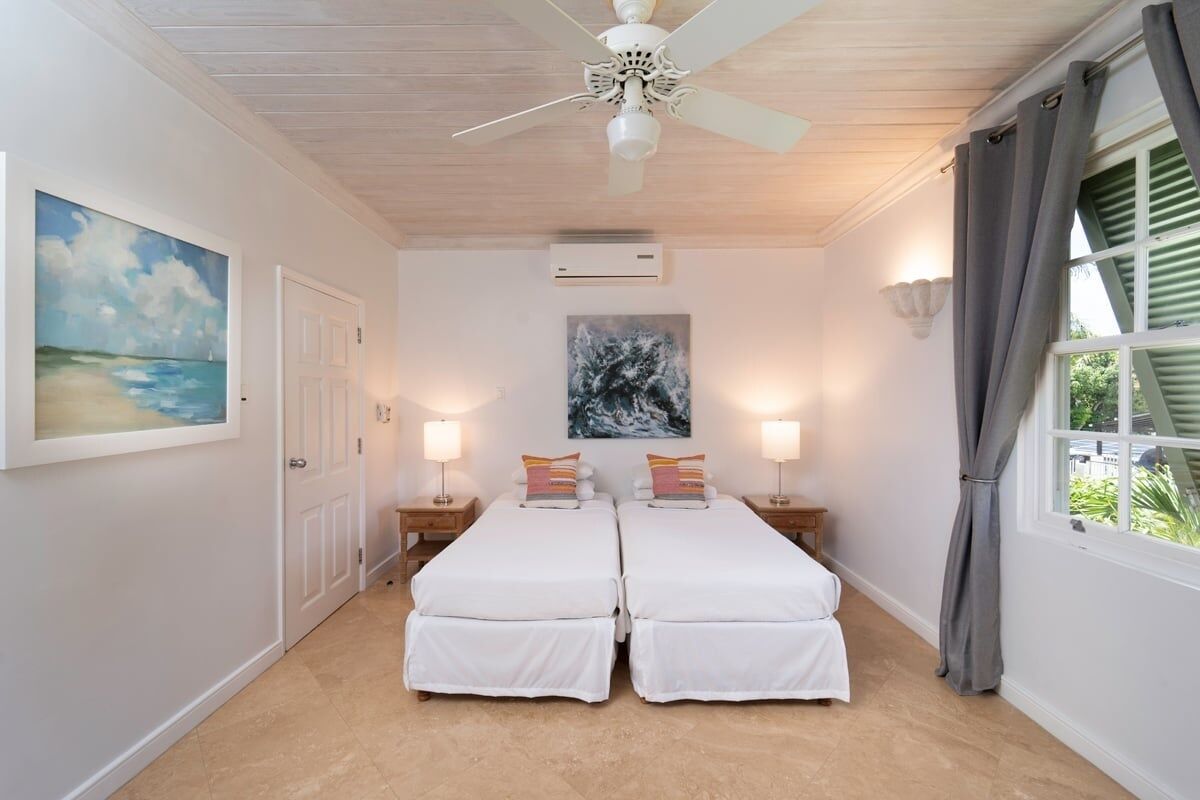 A bedroom with two beds, a ceiling fan, a painting, and a window with curtains.