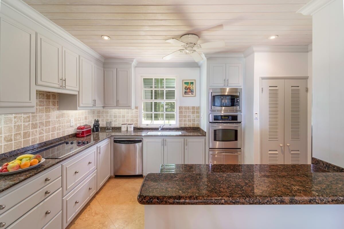 A kitchen with white cabinets, granite countertops, a dishwasher, a microwave, and a ceiling fan.
