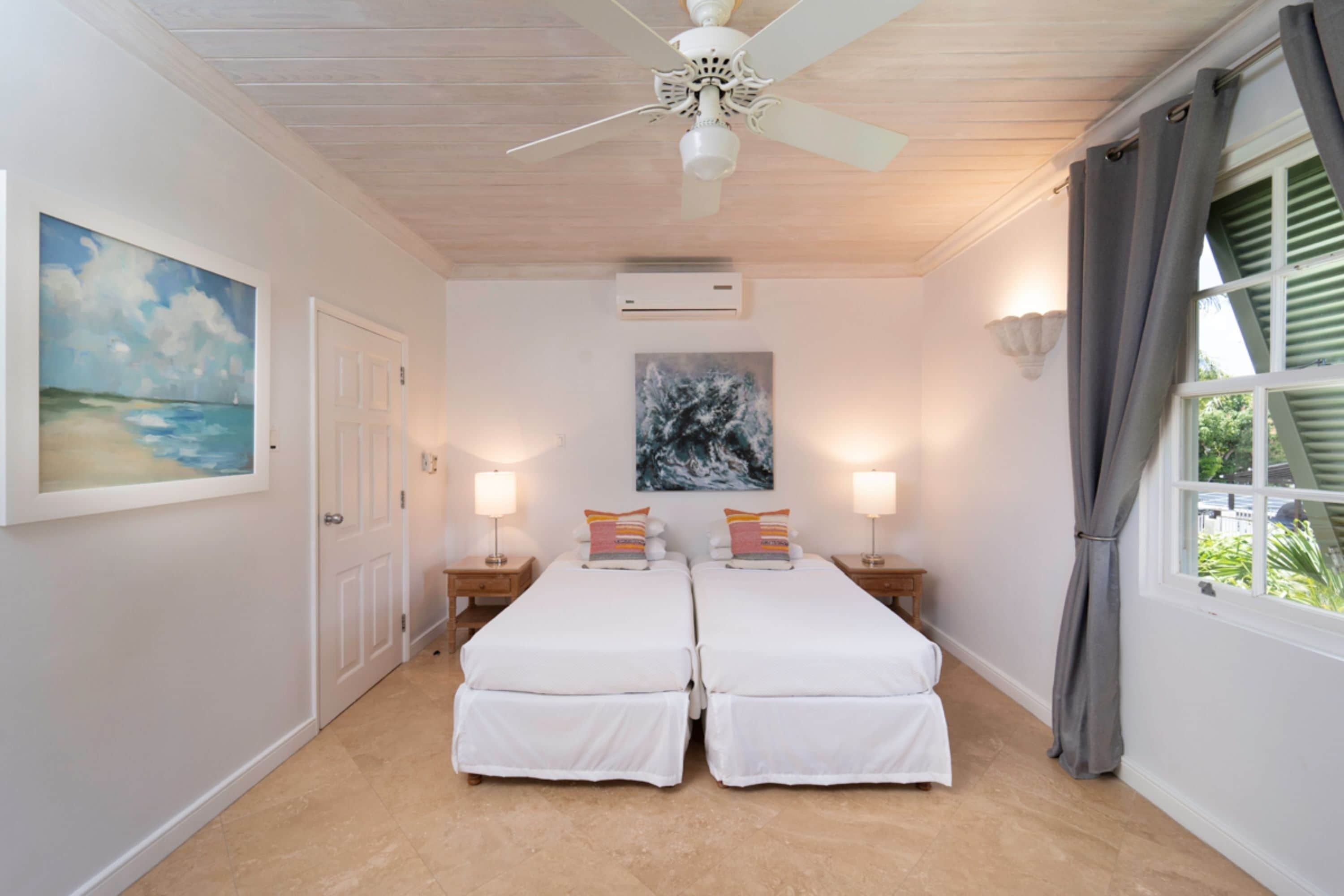 A bedroom with two beds, a ceiling fan, a painting, and a window with curtains.