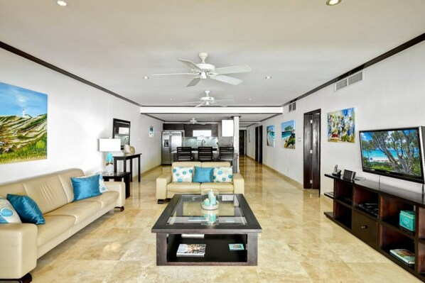 A spacious living room with a beige sofa, a glass coffee table, and a television on the right. - Coral Cove 7 - Sunset by Blue Sky Luxury (Paynes Bay)