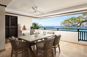 A balcony with a dining table, wicker chairs, and a view of the ocean. - Coral Cove 7 - Sunset by Blue Sky Luxury (Paynes Bay)