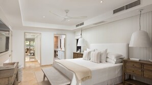 Un dormitorio con una cama grande, mesitas de noche, un banco, un televisor y un ventilador de techo.