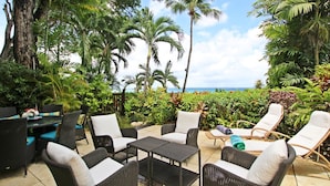 An outdoor patio with wicker furniture, a small table, and a view of the ocean. - Coral Cove 3 - Green Flash Blue Sky Luxury (Paynes Bay)