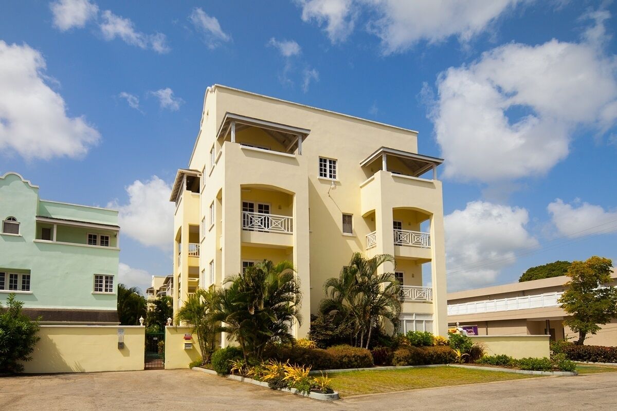 A multi-story hotel with balconies, a parking lot, and surrounding greenery.