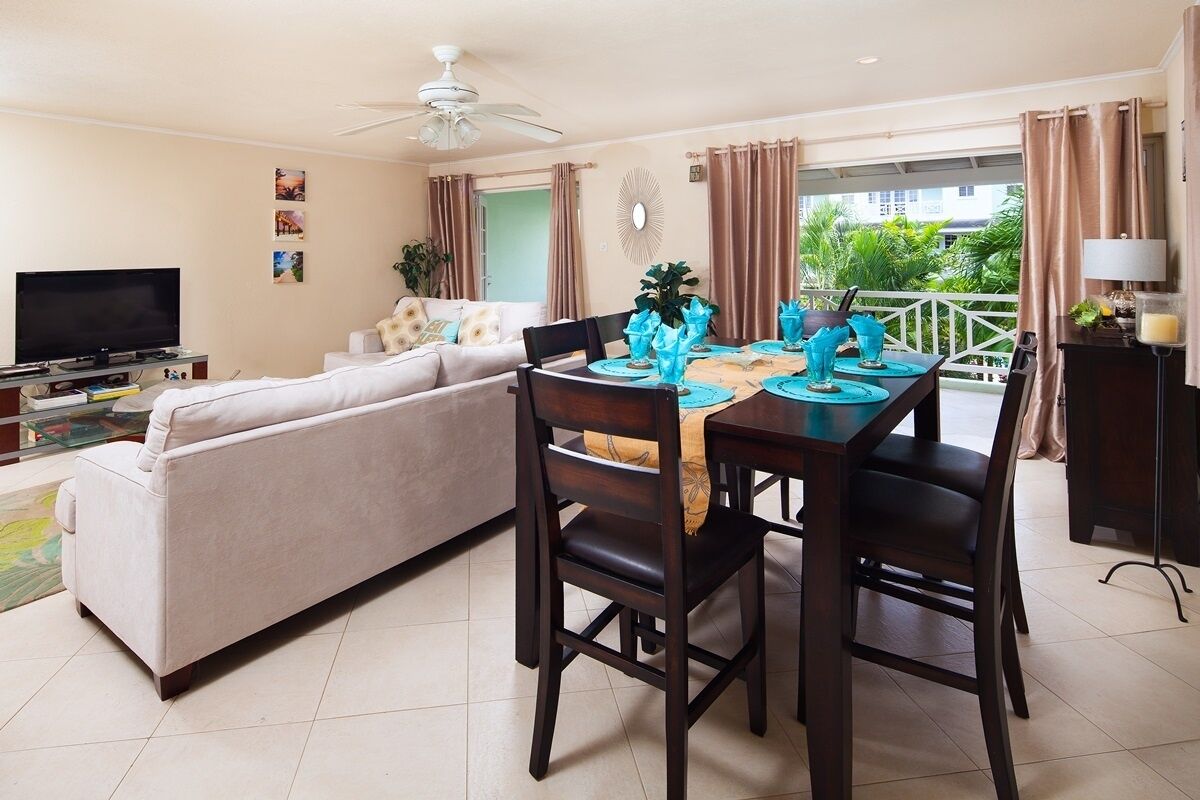 A living room with a sofa, a dining table set for four, a TV, and a ceiling fan.